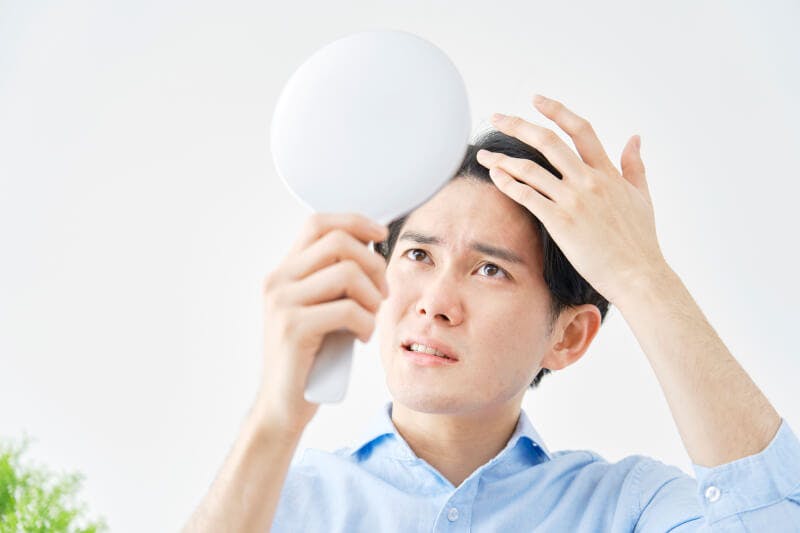 ハンドミラーで生え際の様子を確認している男性