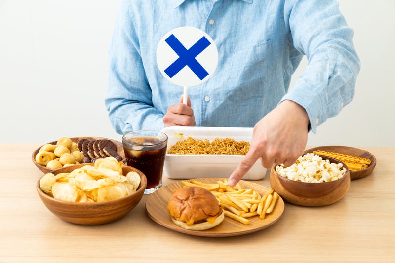 多数のジャンクフードを前に、バツのプラカードを持つ男性