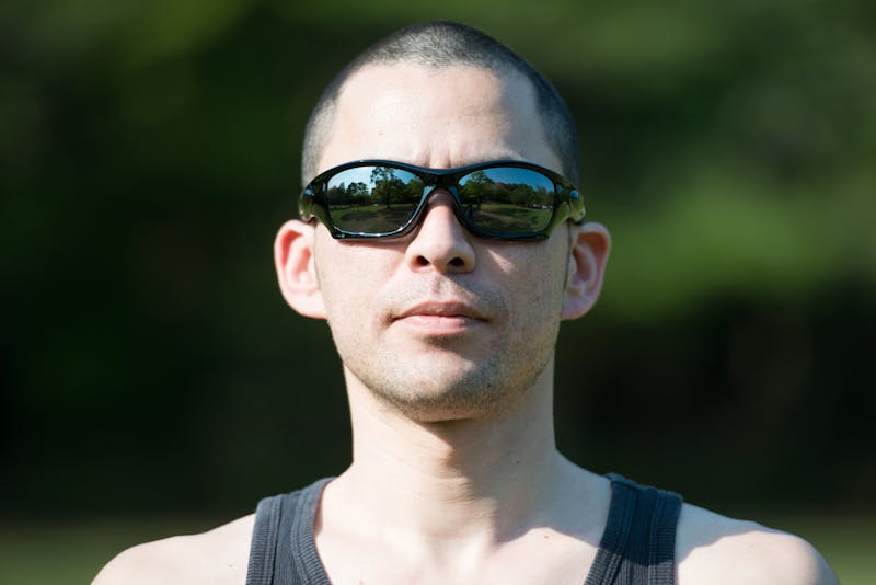 晴天下、サングラスをかけて眉間にシワを寄せた丸坊主の男性