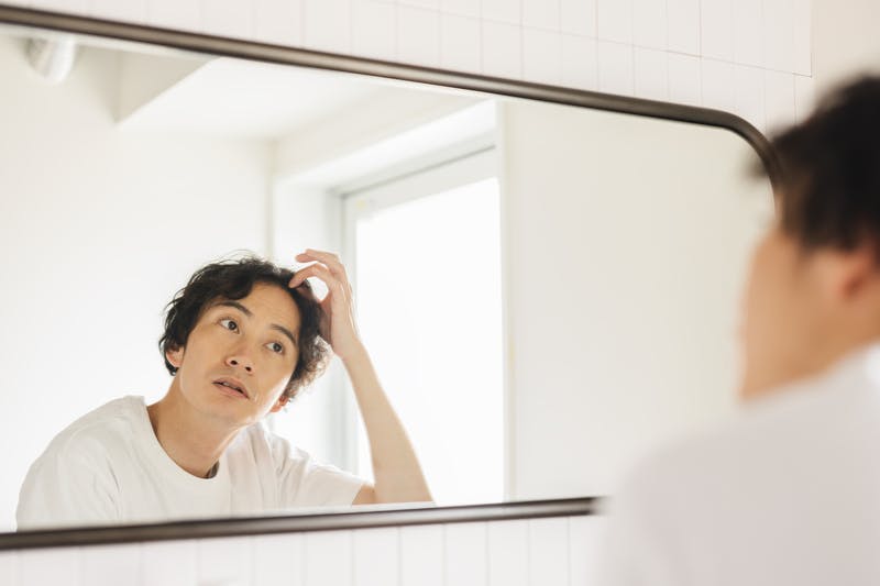 鏡の前で毛髪の様子をチェックし、何か考えている男性