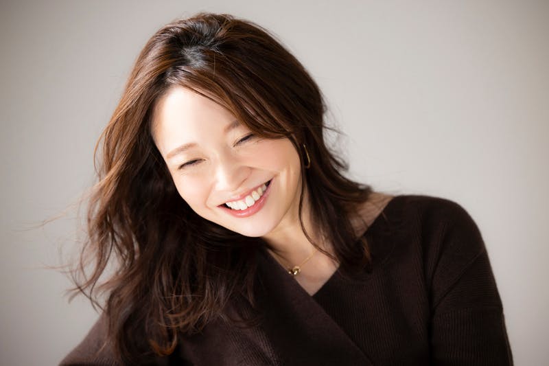 うつむき加減で微笑むロングヘアの女性