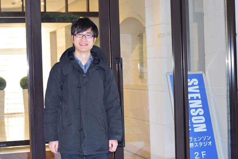 スヴェンソン 上野スタジオの入り口前に立つコクブさん（笑顔）