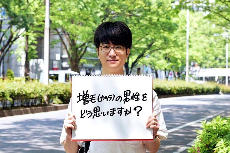 スヴェンソンの増毛愛用者・コクブさん　「増毛（カツラ）の男性をどう思いますか？」のフリップを持っている様子。