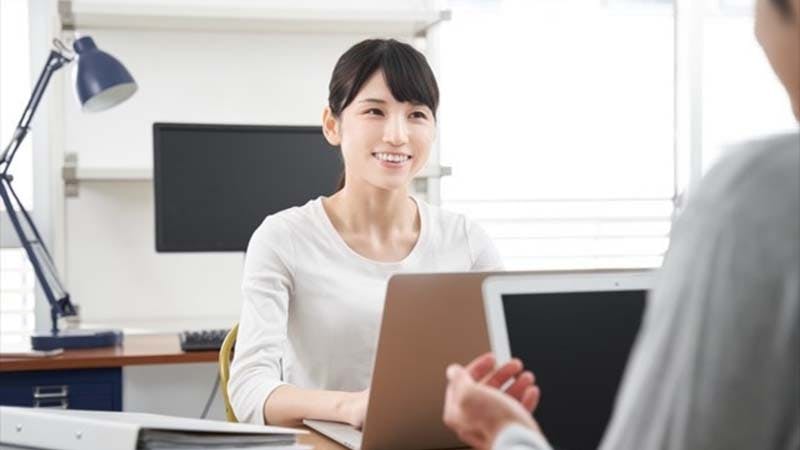 仕事中、男性と話しながら微笑む女性