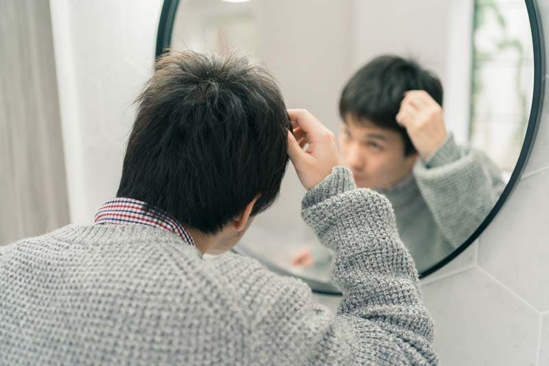鏡を見ながら髪型を気にしている男性のイメージ画像