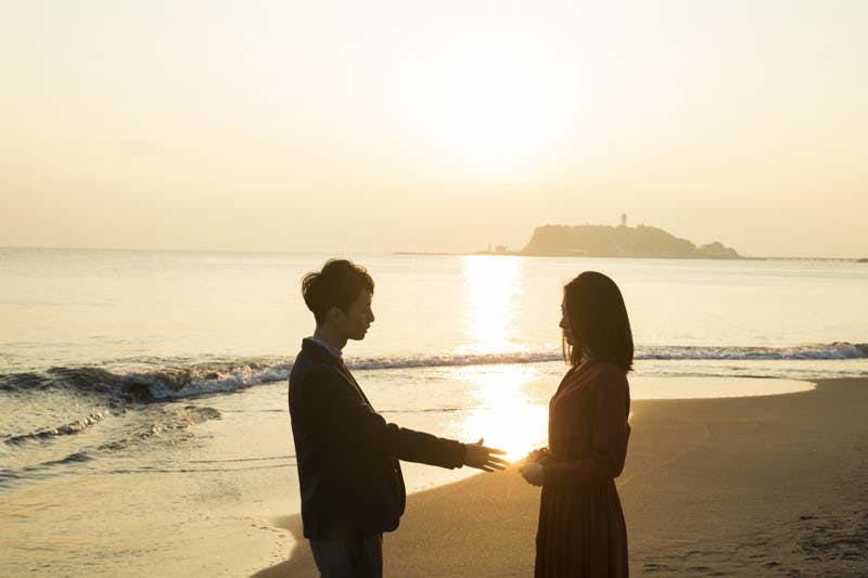 海辺で彼女にプロポーズする男性のイメージ画像