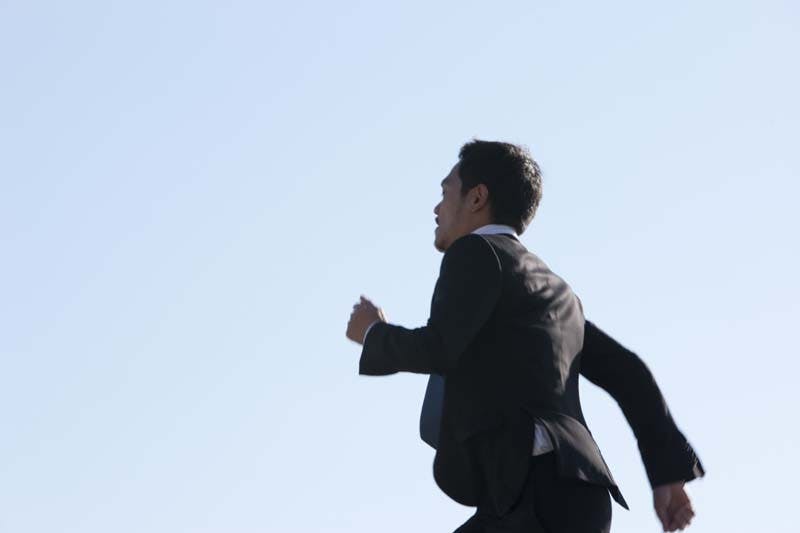 青空の下をスーツ姿で駆け抜ける男性のイメージ画像