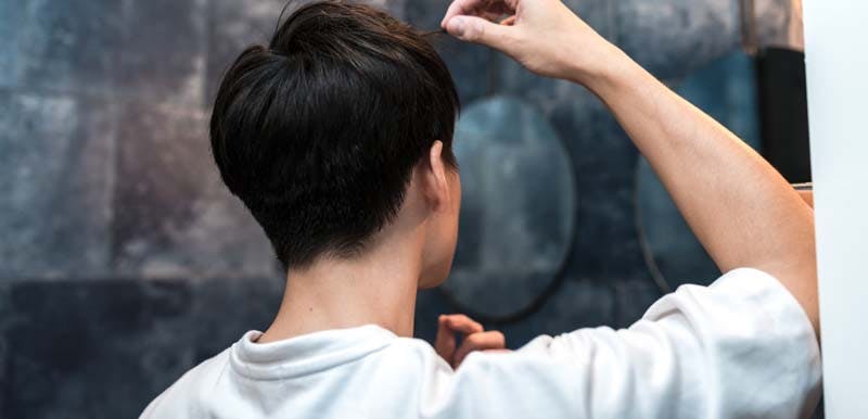 鏡を見ながら髪型を調整する男性のイメージ画像