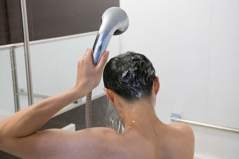 シャワーを頭からかぶって湯シャンする男性のイメージ画像