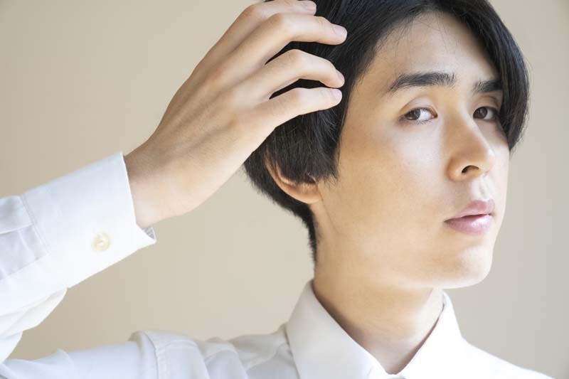前髪の生え際を気にしている長髪の男性のイメージ画像