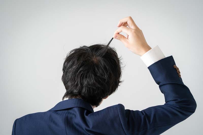 髪の毛に触れながら首をかしげる男性のイメージ画像