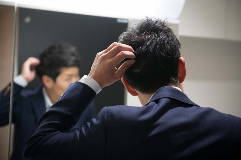 鏡を覗いて後頭部の薄毛を気にする男性のイメージ画像