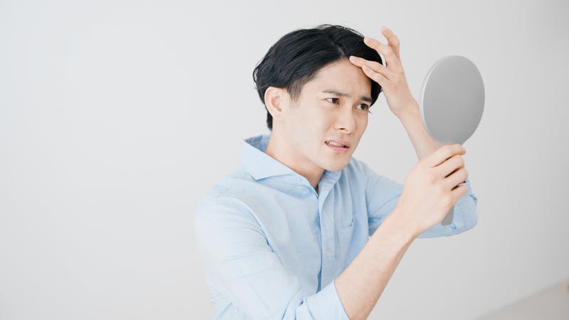 鏡を見て生え際の様子を確認している男性