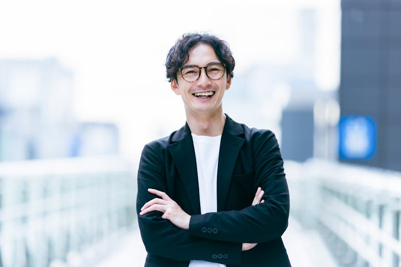 パーマをかけてセンター分けにし、カメラ目線で笑いかける男性