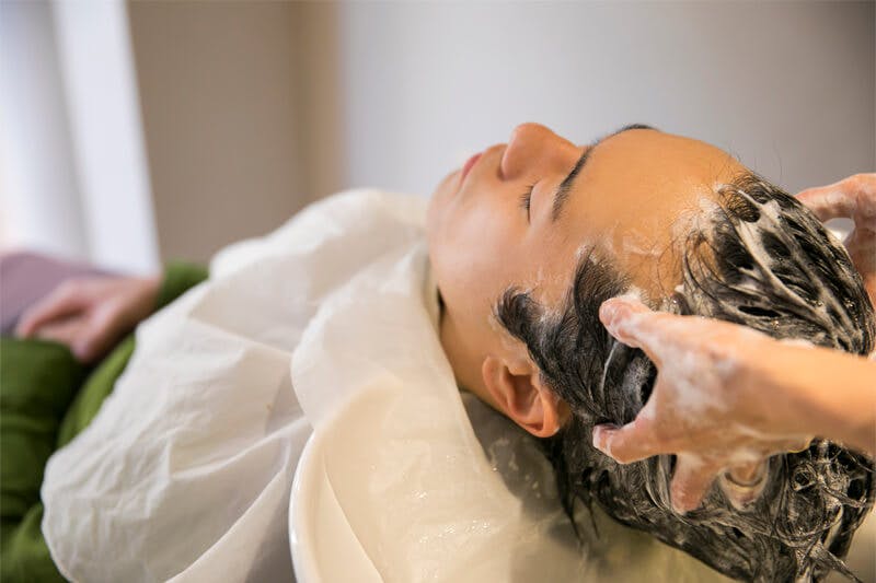 シャンプー台に頭を乗せ、目を閉じて洗髪してもらう男性