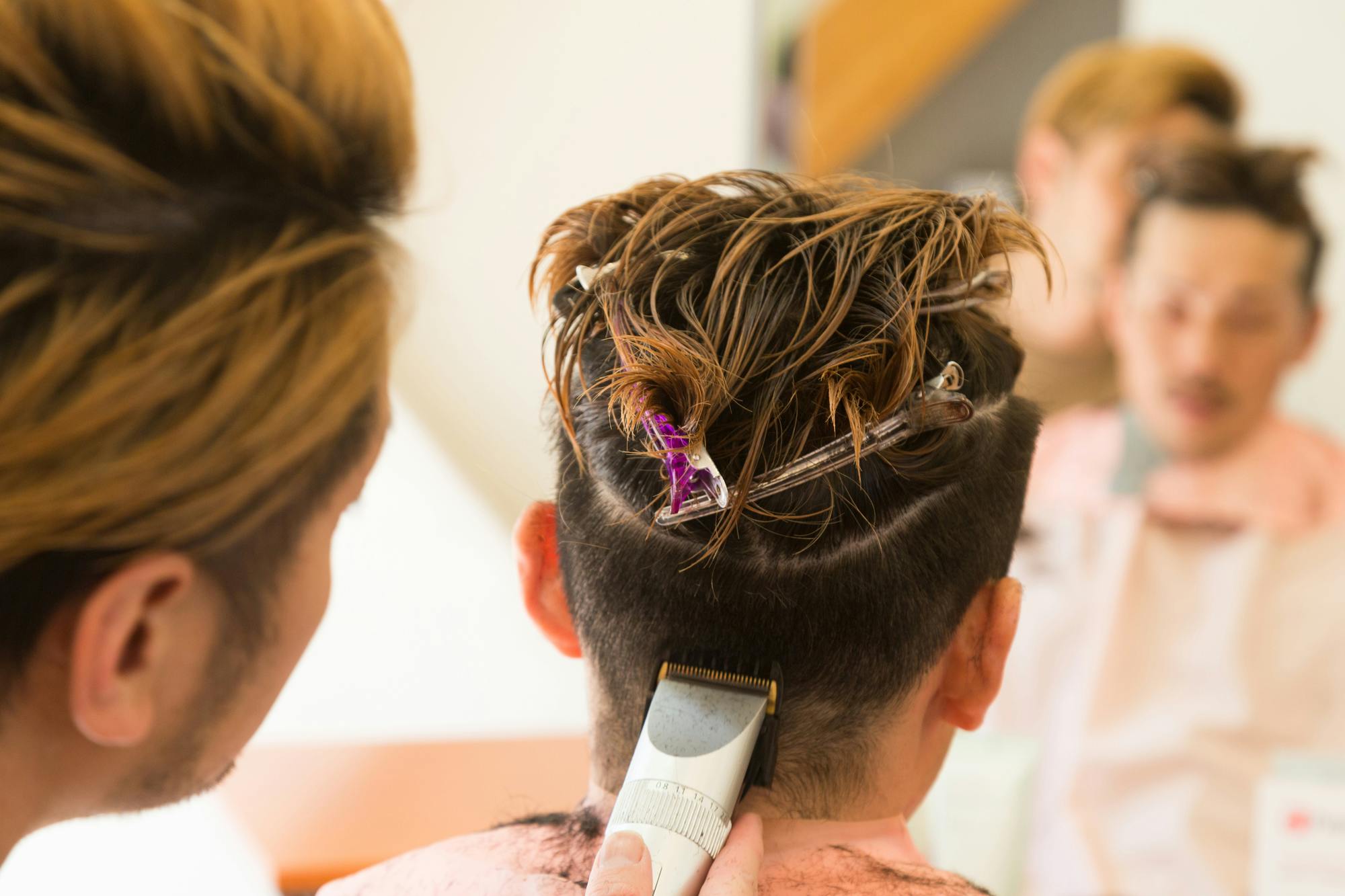 頭頂部をブロッキングした男性の側頭部と後頭部をバリカンで刈り上げる美容師