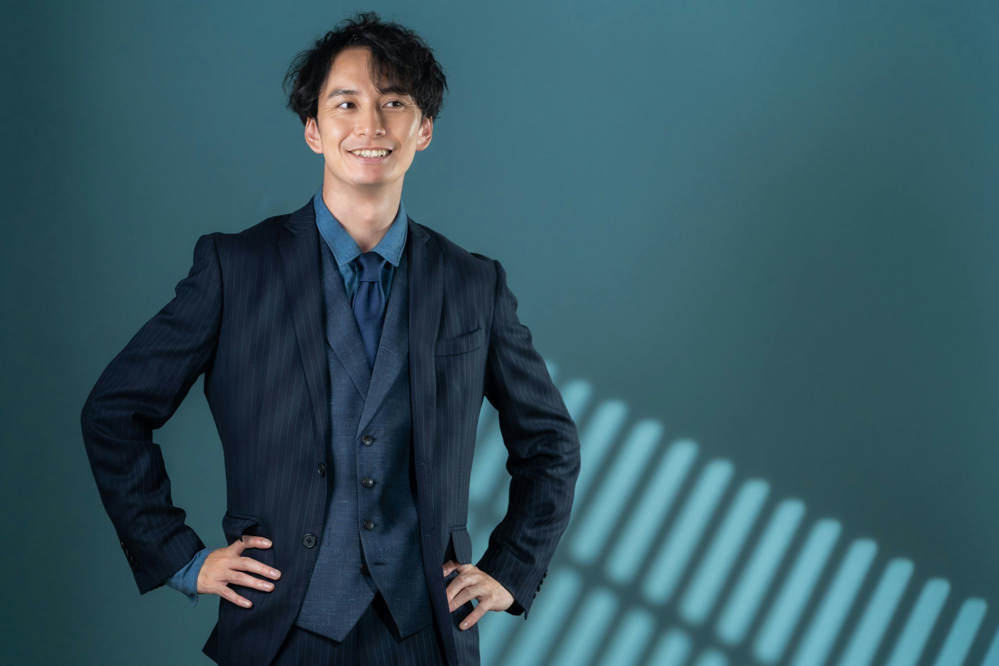 腰に手を当て自信ありげに微笑む、スーツスタイルの男性