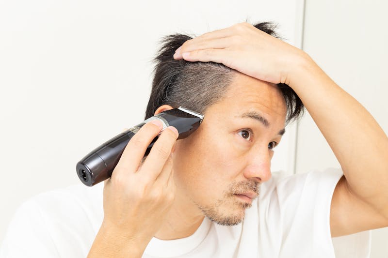 バリカンで自分の側頭部を刈り上げる男性