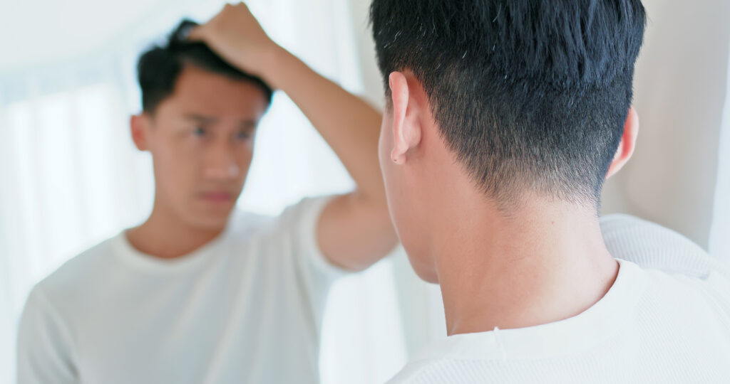鏡を見ながらおでこと生え際を確認している男性