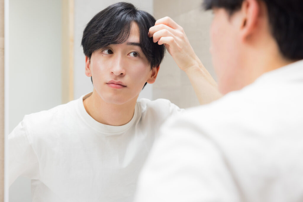 鏡を見ながらおでこと生え際を確認している男性