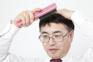 ピンクのヘアブラシでかつらをブラッシングする男性