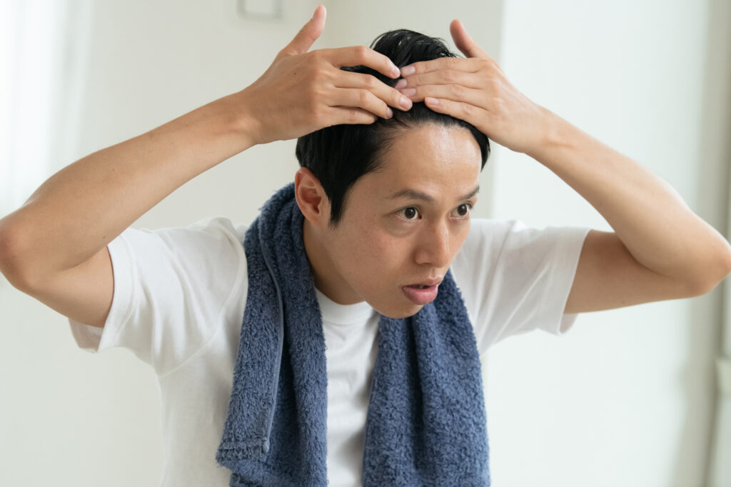 首にタオルをかけ、頭皮や髪の状態を両手で確認・ケアする男性