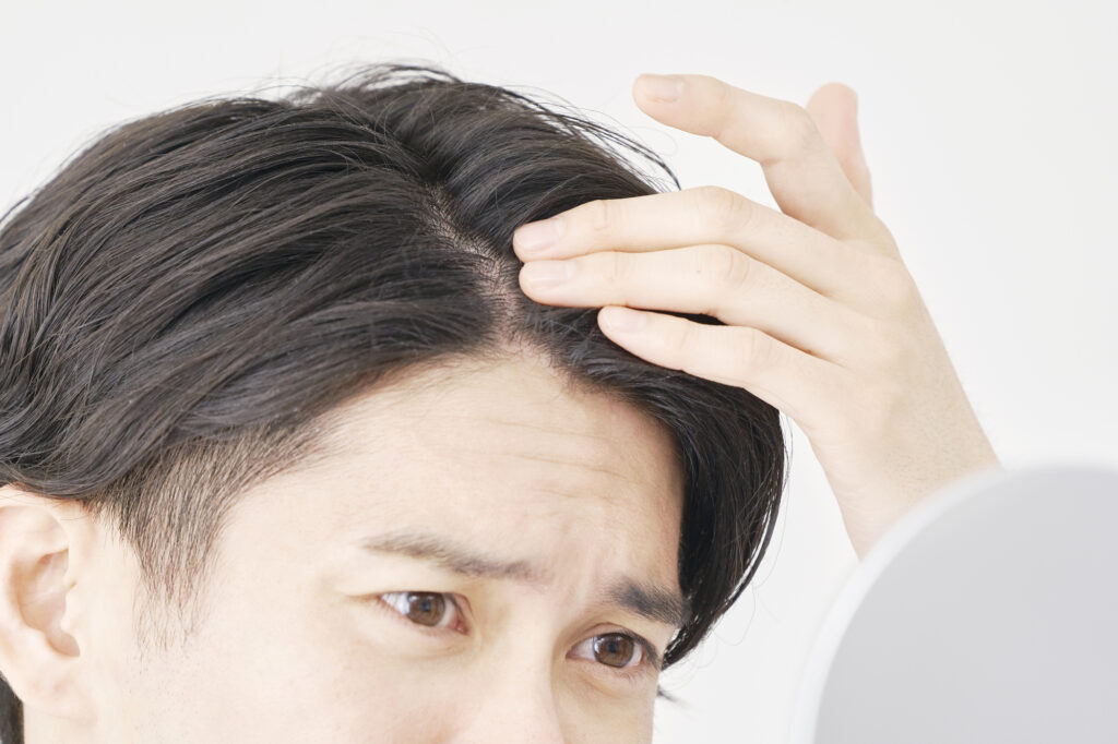 ハンドミラーで分け目の様子を念入りに確認している男性