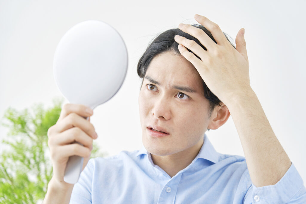 手鏡を持って生え際を気にする男性